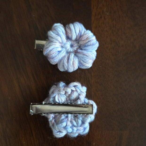 Two handmade light purple crochet flower hair clips on a dark wooden surface