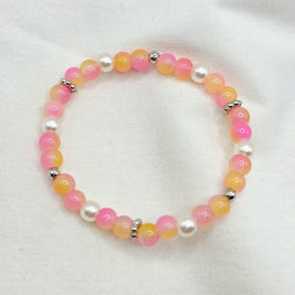 Pink and orange beaded bracelet with pearl accents on white fabric