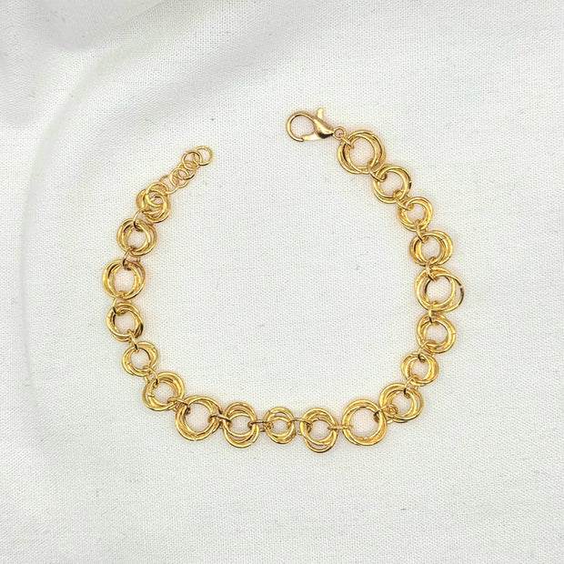Gold tone interlocking circle bracelet with lobster clasp on white fabric background