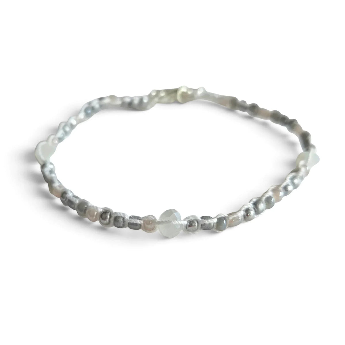 Delicate beaded bracelet with silver, gray, and white beads on white fabric background