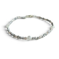 Delicate beaded bracelet with silver, gray, and white beads on white fabric background