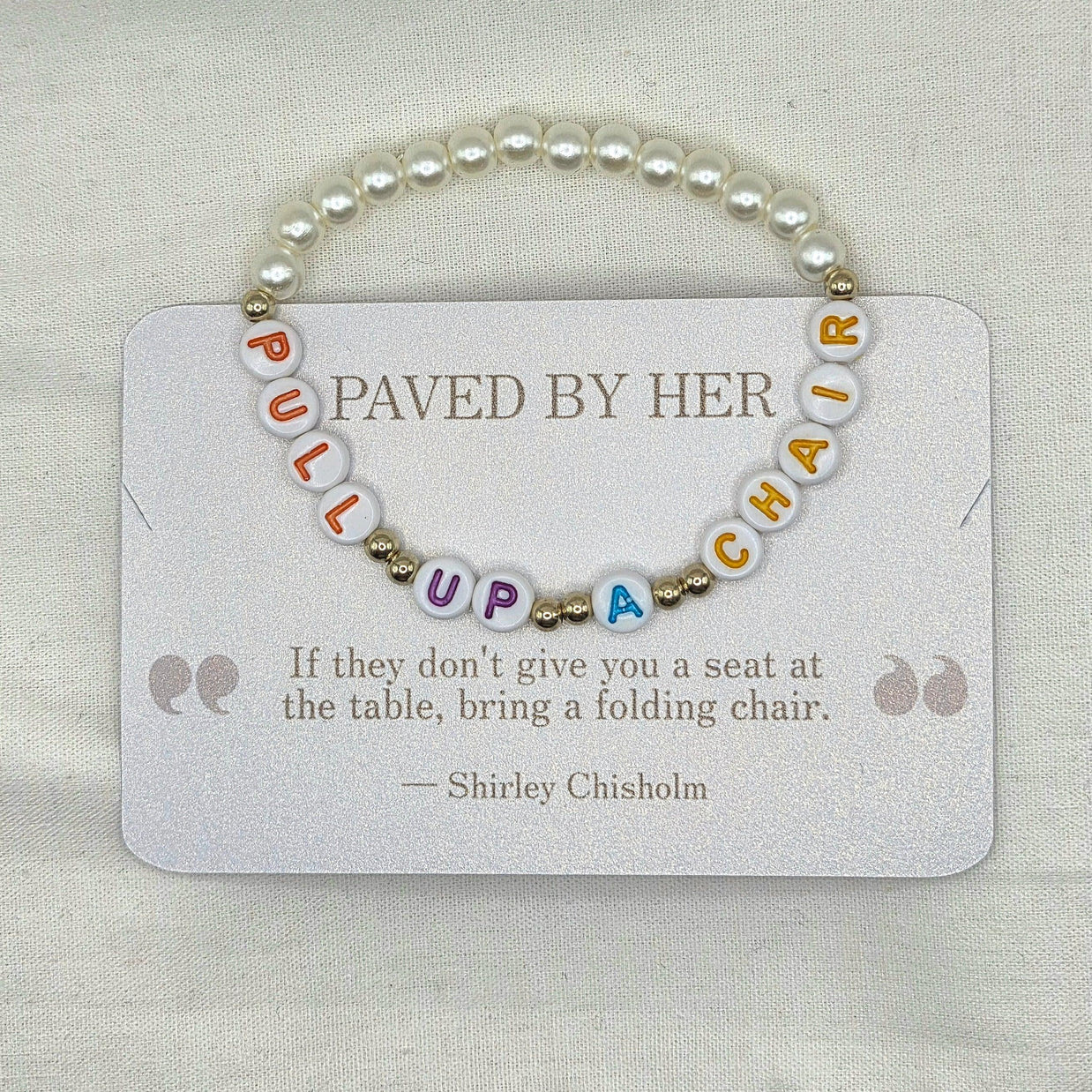 Pearl bracelet with 'PULL UP A CHAIR' letter beads on a card with Shirley Chisholm quote