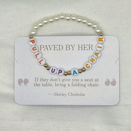 Pearl bracelet with 'PULL UP A CHAIR' letter beads on a card with Shirley Chisholm quote