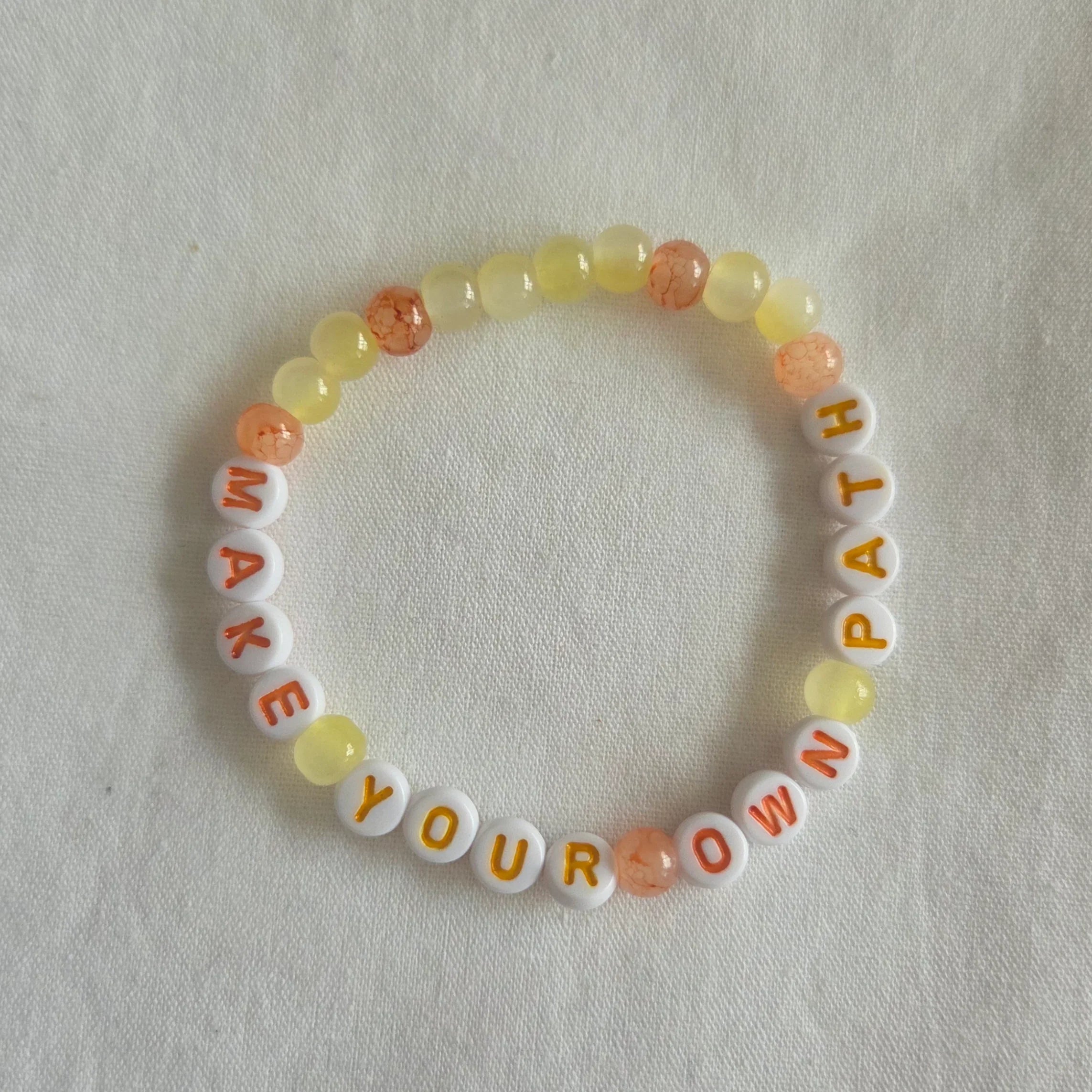 Make Your Own Path beaded bracelet with yellow and orange beads on white fabric