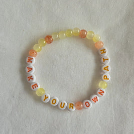 Make Your Own Path beaded bracelet with yellow and orange beads on white fabric