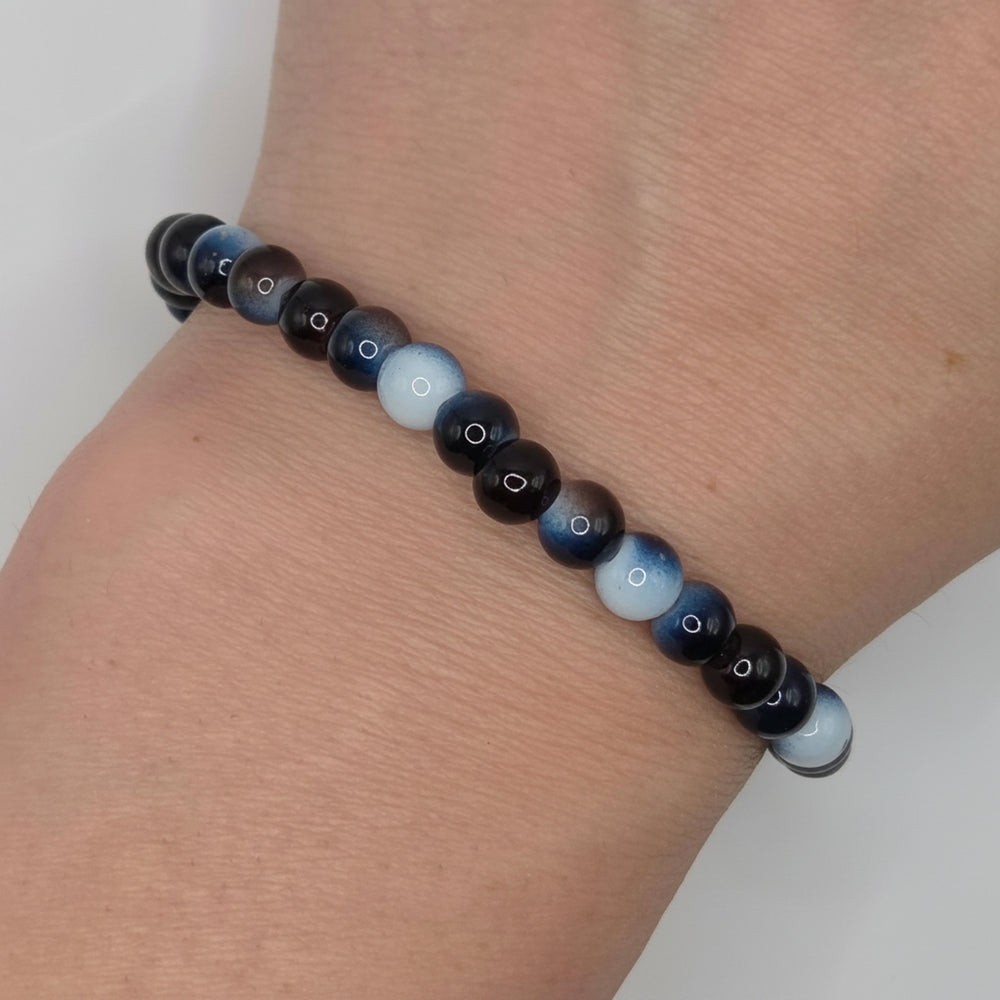 A beaded stretch bracelet with glossy round beads in black, dark blue, and light blue with white star details, shown worn on a person's wrist.