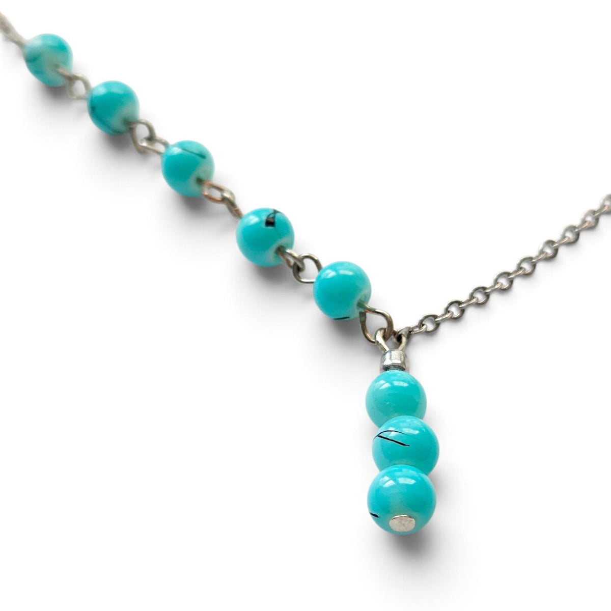 A silver chain necklace featuring a horizontal bar with small turquoise beads and a vertical drop of three larger turquoise beads, shown on a white background.