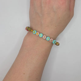 Handmade beaded bracelet spelling 'MEANXIOUS' in pastel and gold letters, worn on wrist