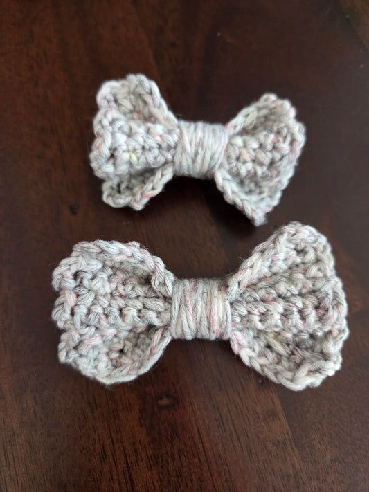Two handmade crochet bows in light yarn on a dark wooden surface