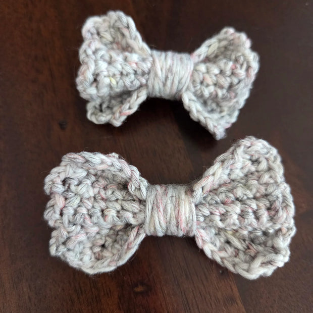 Two handmade crochet bows in light yarn on a dark wooden surface