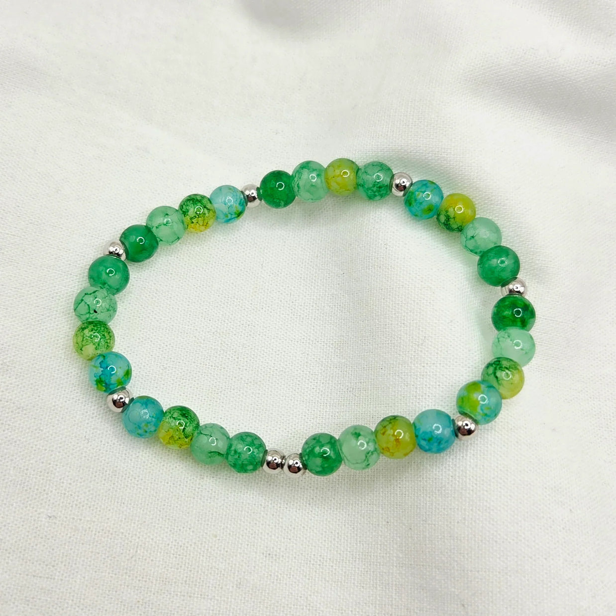 Green and blue marbled bead bracelet with silver accents on white fabric