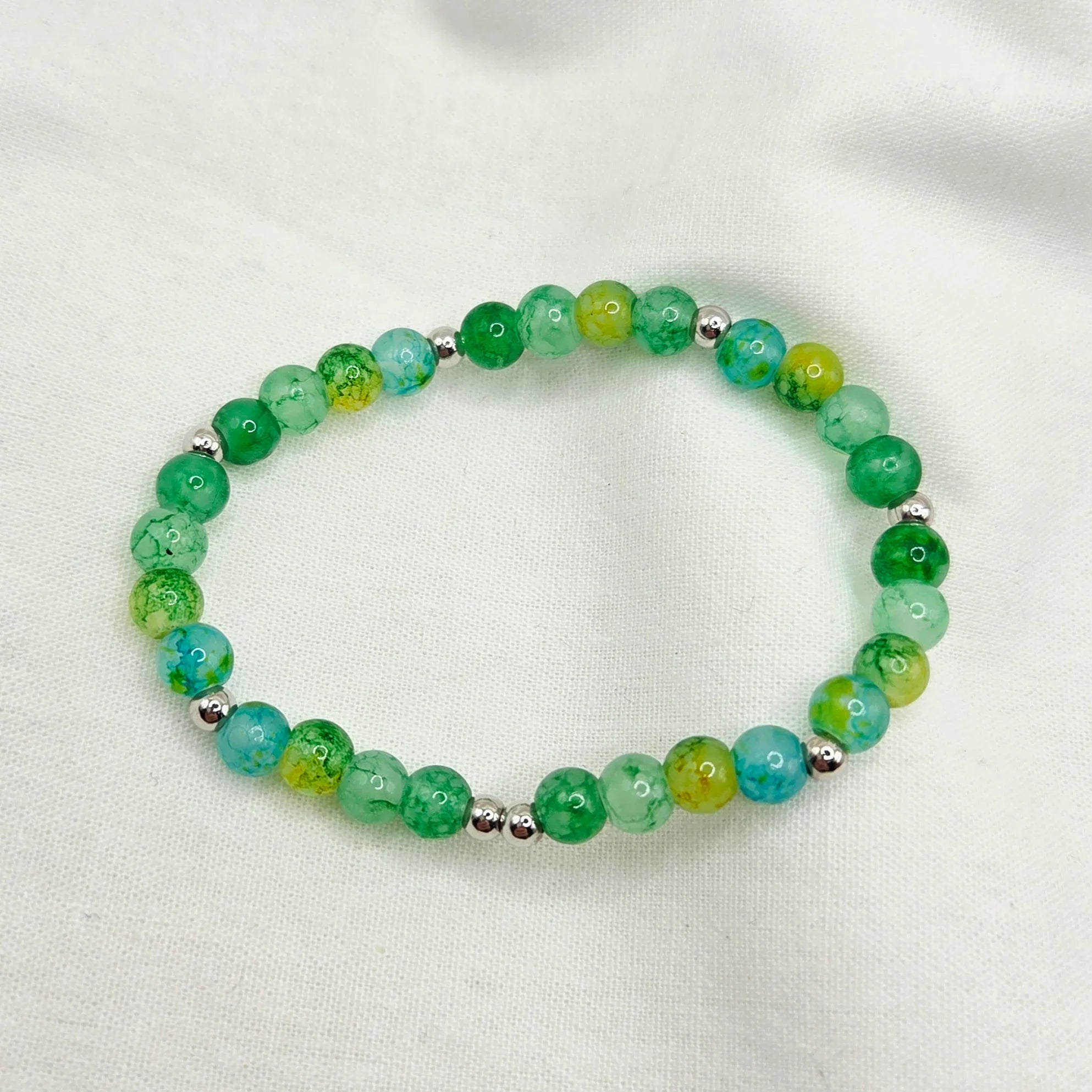 Green and blue marbled bead bracelet with silver accents on white fabric