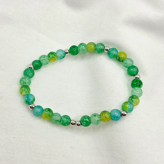 Green and blue marbled bead bracelet with silver accents on white fabric