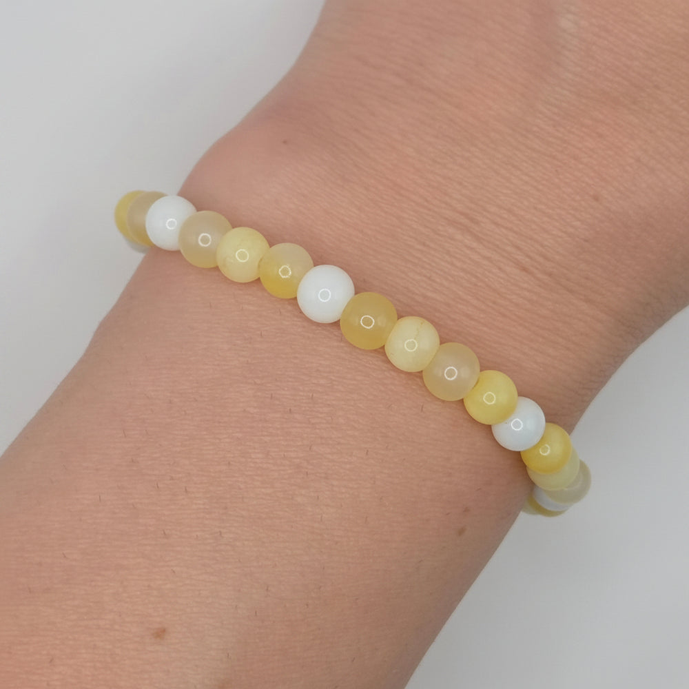 A beaded stretch bracelet made of round matte beads in pale yellow and white, shown worn on a person's wrist against a light neutral background.