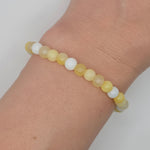 A beaded stretch bracelet made of round matte beads in pale yellow and white, shown worn on a person's wrist against a light neutral background.
