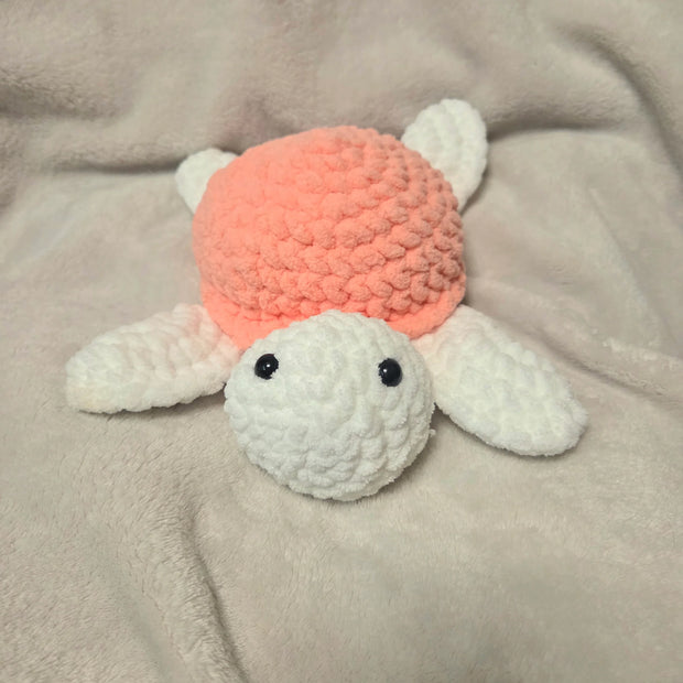 Handmade crochet turtle plushie with pink shell and white body on cozy blanket