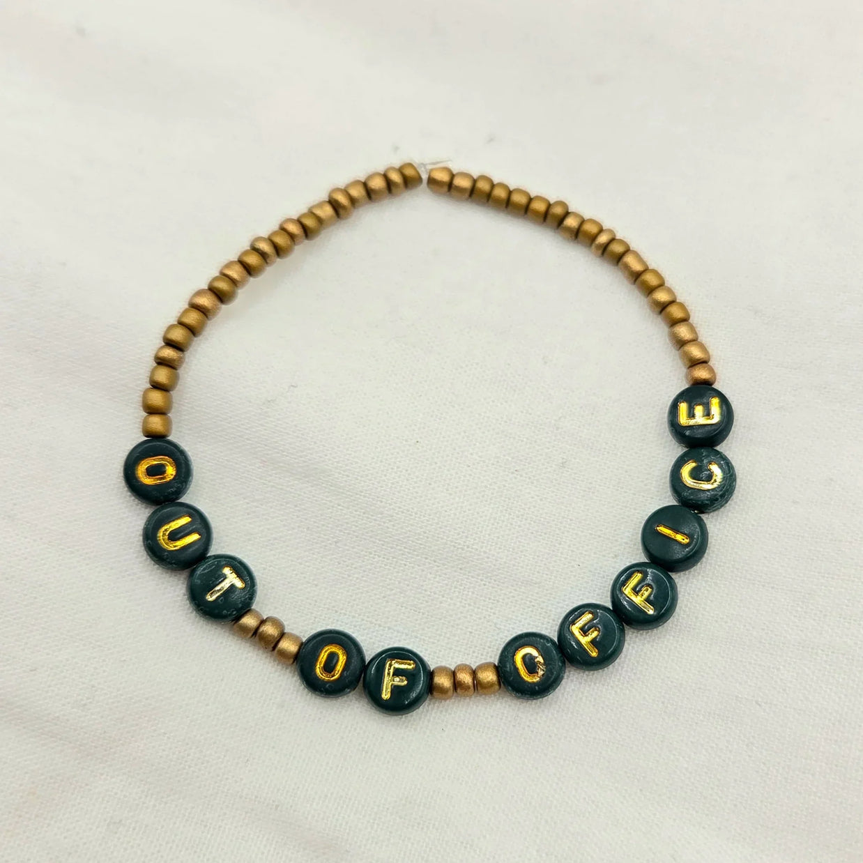 Handmade 'OUT OF OFFICE' beaded bracelet with green and gold letter beads, perfect for cozy, creative gifts.