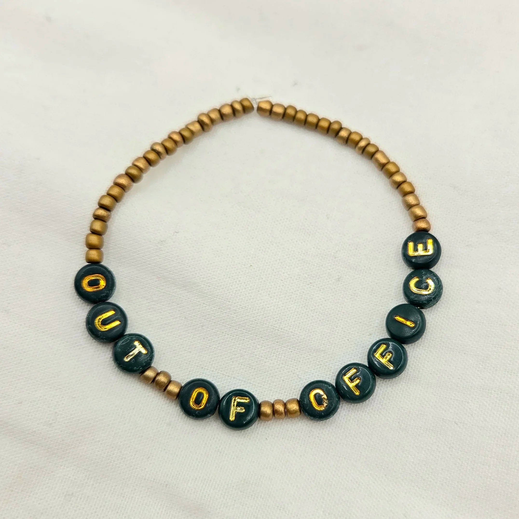 Handmade 'OUT OF OFFICE' beaded bracelet with green and gold letter beads, perfect for cozy, creative gifts.