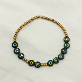 Handmade 'OUT OF OFFICE' beaded bracelet with green and gold letter beads, perfect for cozy, creative gifts.