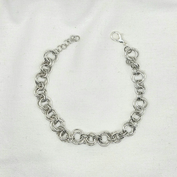Silver chainmaille bracelet with interlocking rings and lobster clasp on white fabric