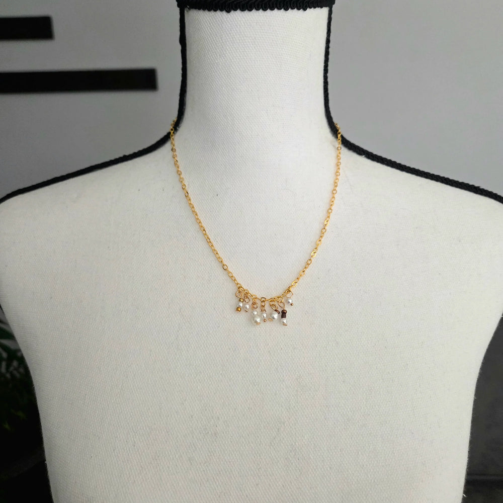 Delicate gold chain necklace with pearl and bead charms, displayed on a mannequin.