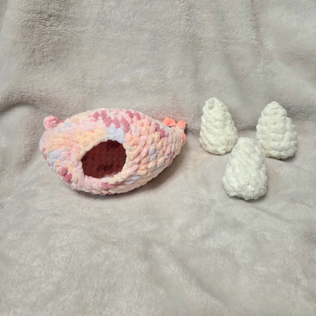 Handmade crochet pet cave with pastel pink and white design, cozy for small pets, accompanied by white crochet trees.