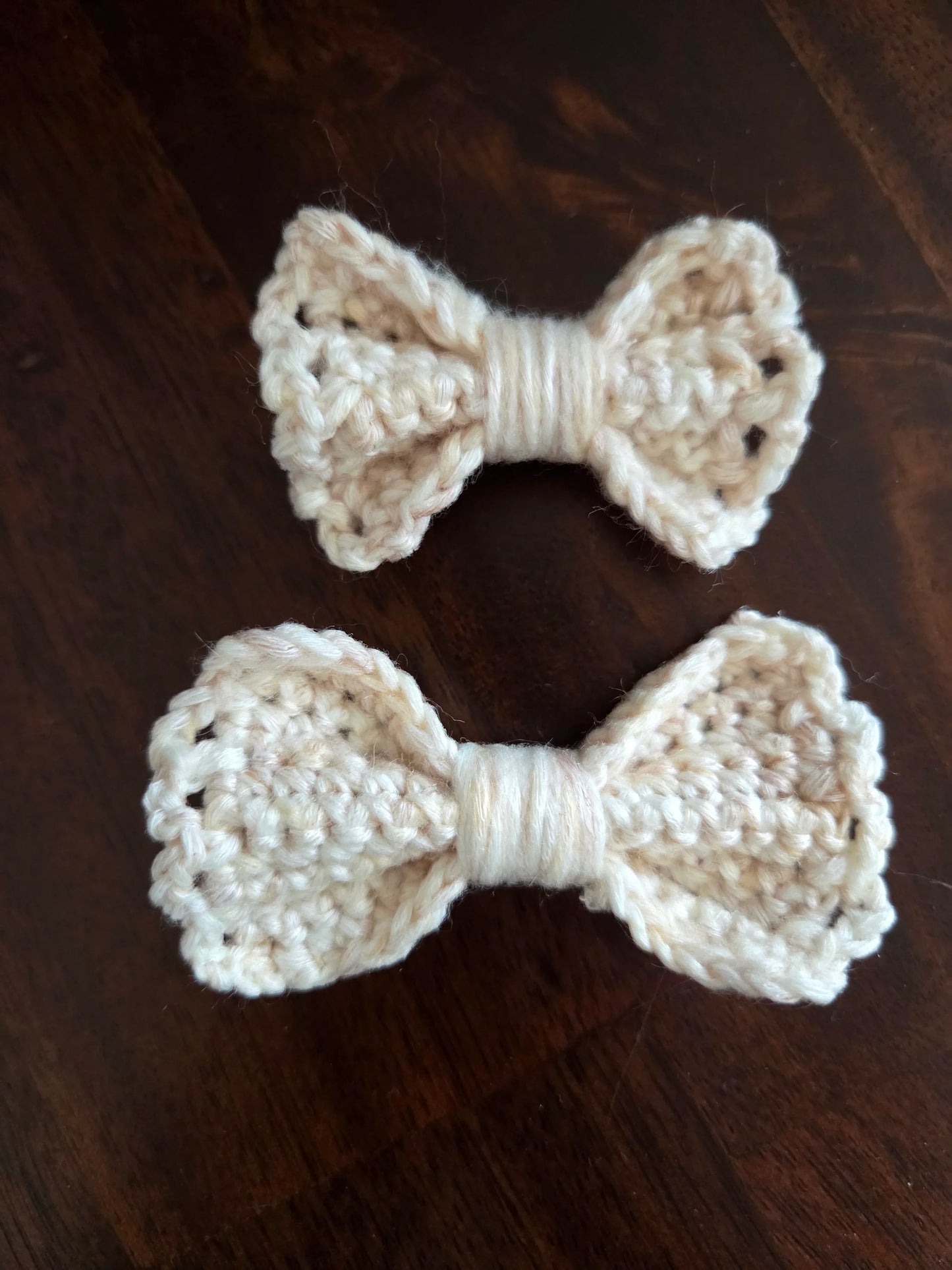 Two handmade cream crochet bows on a dark wooden surface