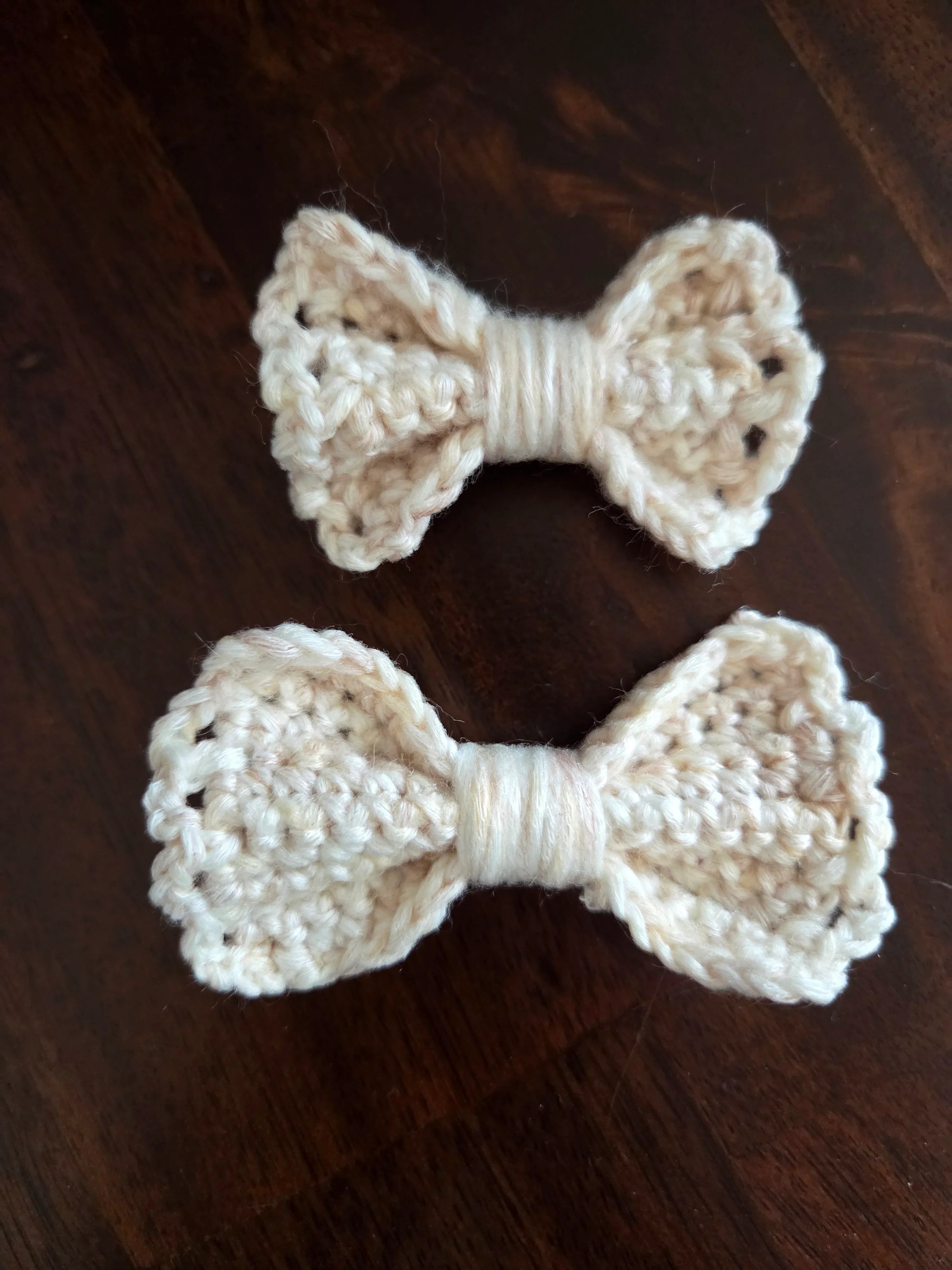 Two handmade cream crochet bows on a dark wooden surface
