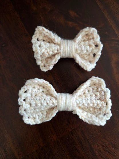 Two handmade cream crochet bows on a dark wooden surface