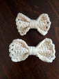Two handmade cream crochet bows on a dark wooden surface