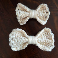 Two handmade cream crochet bows on a dark wooden surface