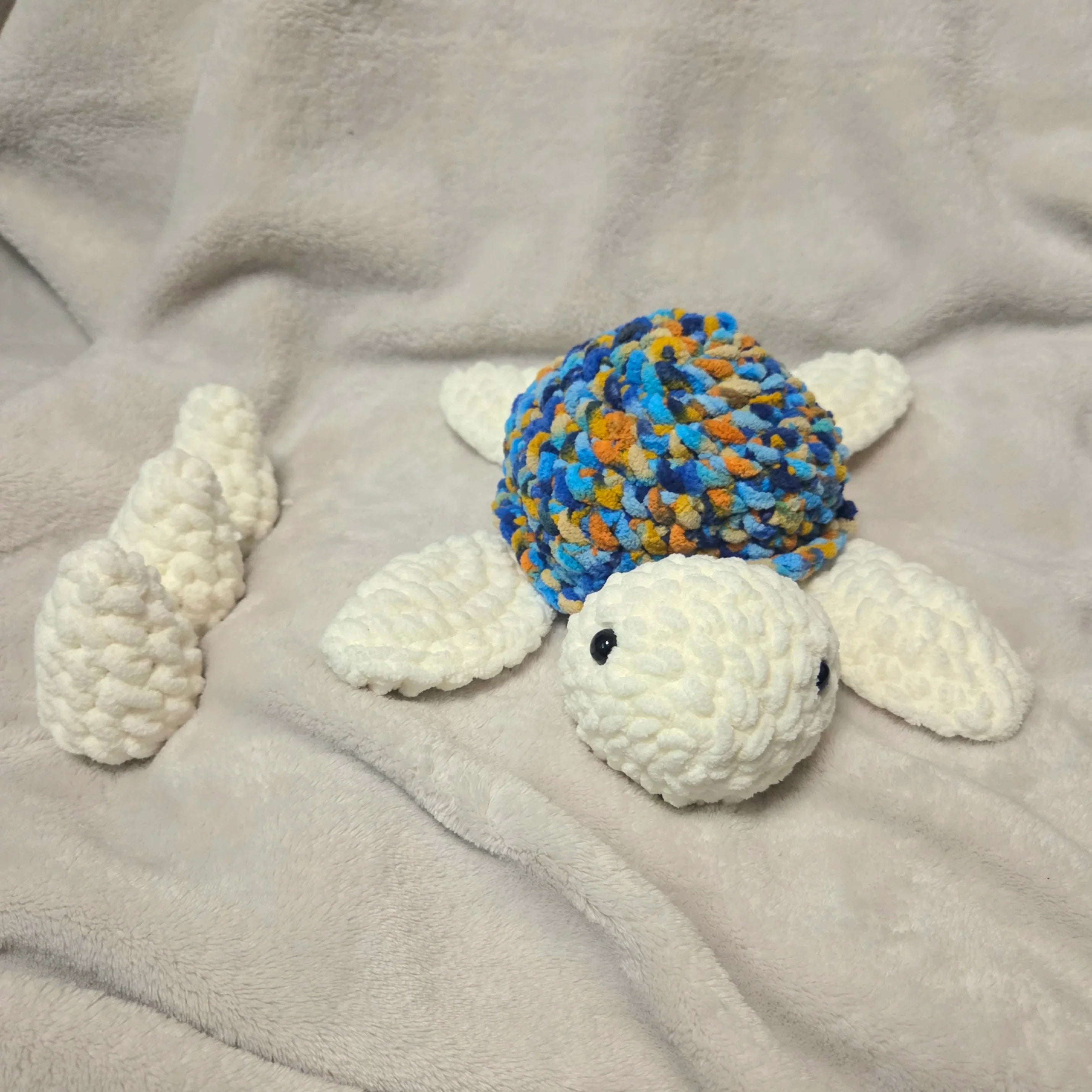 Handmade crochet turtle with colorful shell and white limbs on soft blanket