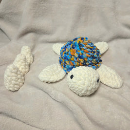 Handmade crochet turtle with colorful shell and white limbs on soft blanket