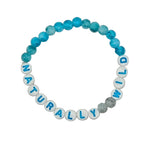 A beaded stretch bracelet on a light gray background. The bracelet features round blue marbled beads and white letter beads spelling 'NATURALLY WILD' with blue letters.